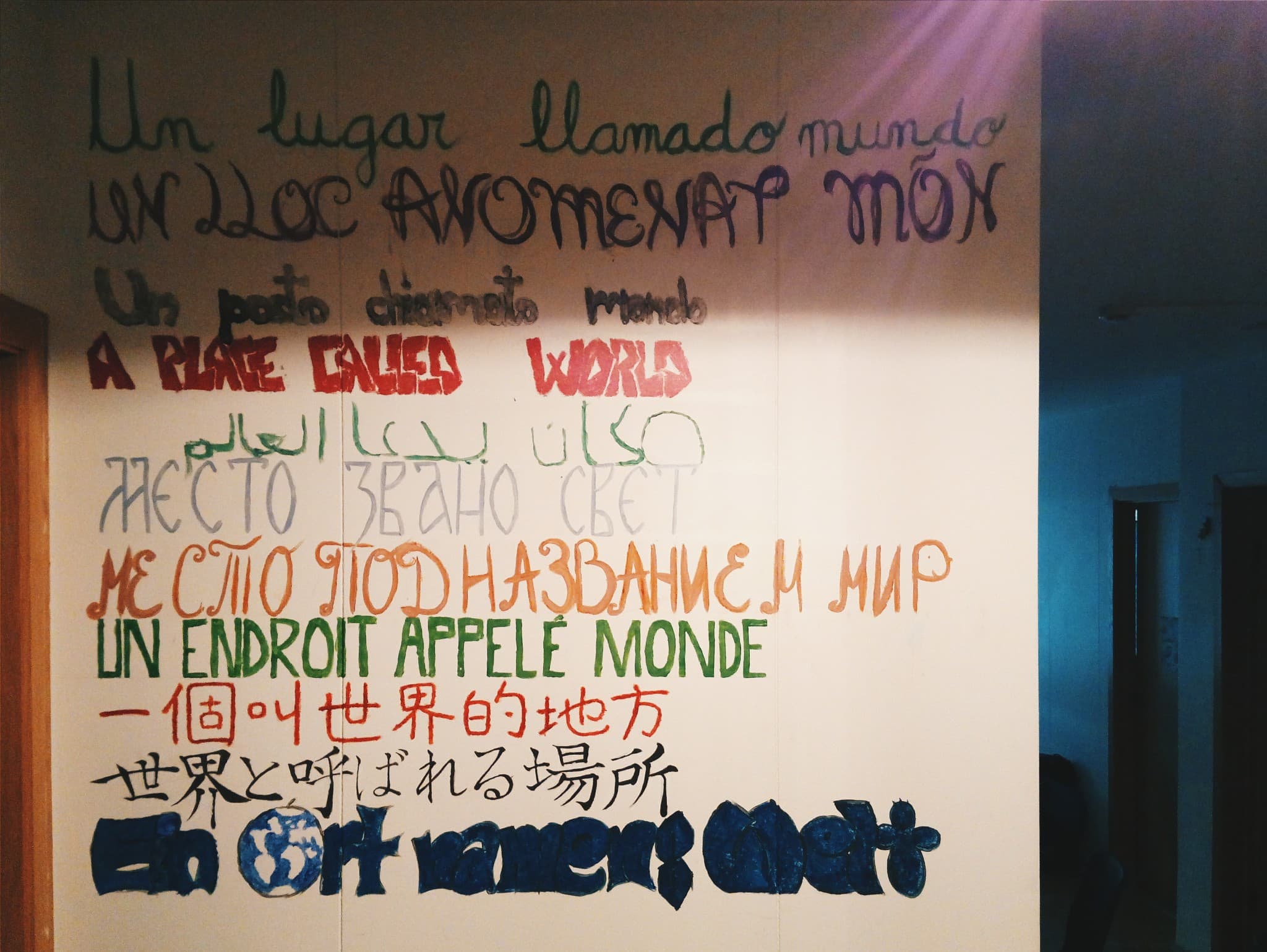 A white wall features the phrase "a place called world" hand-painted in various languages and colors.