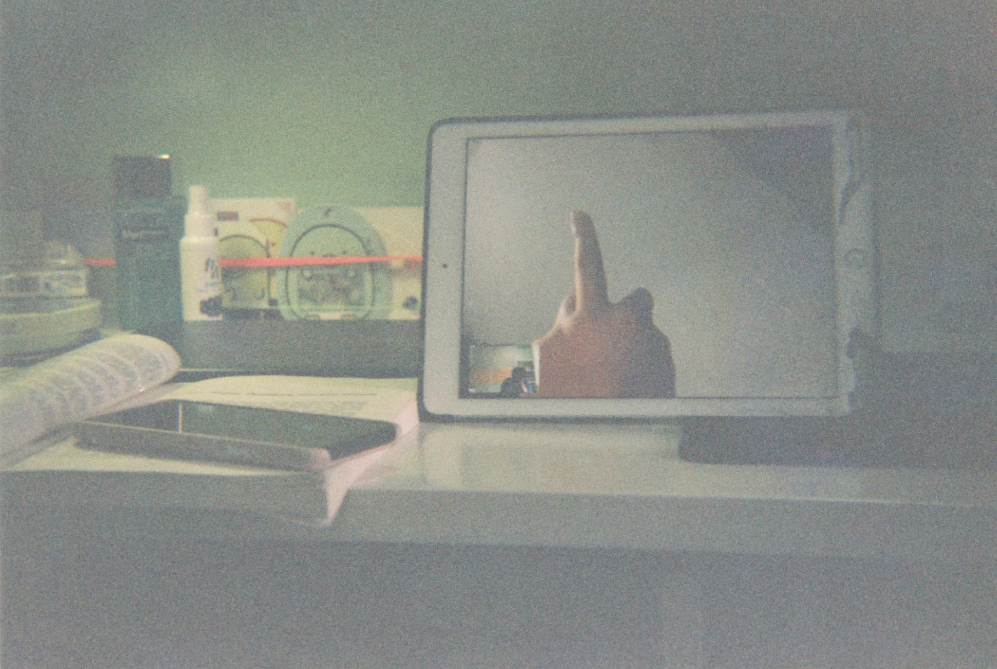 A tablet computer displaying a hand giving the middle finger sits on a desk next to books and bottles.