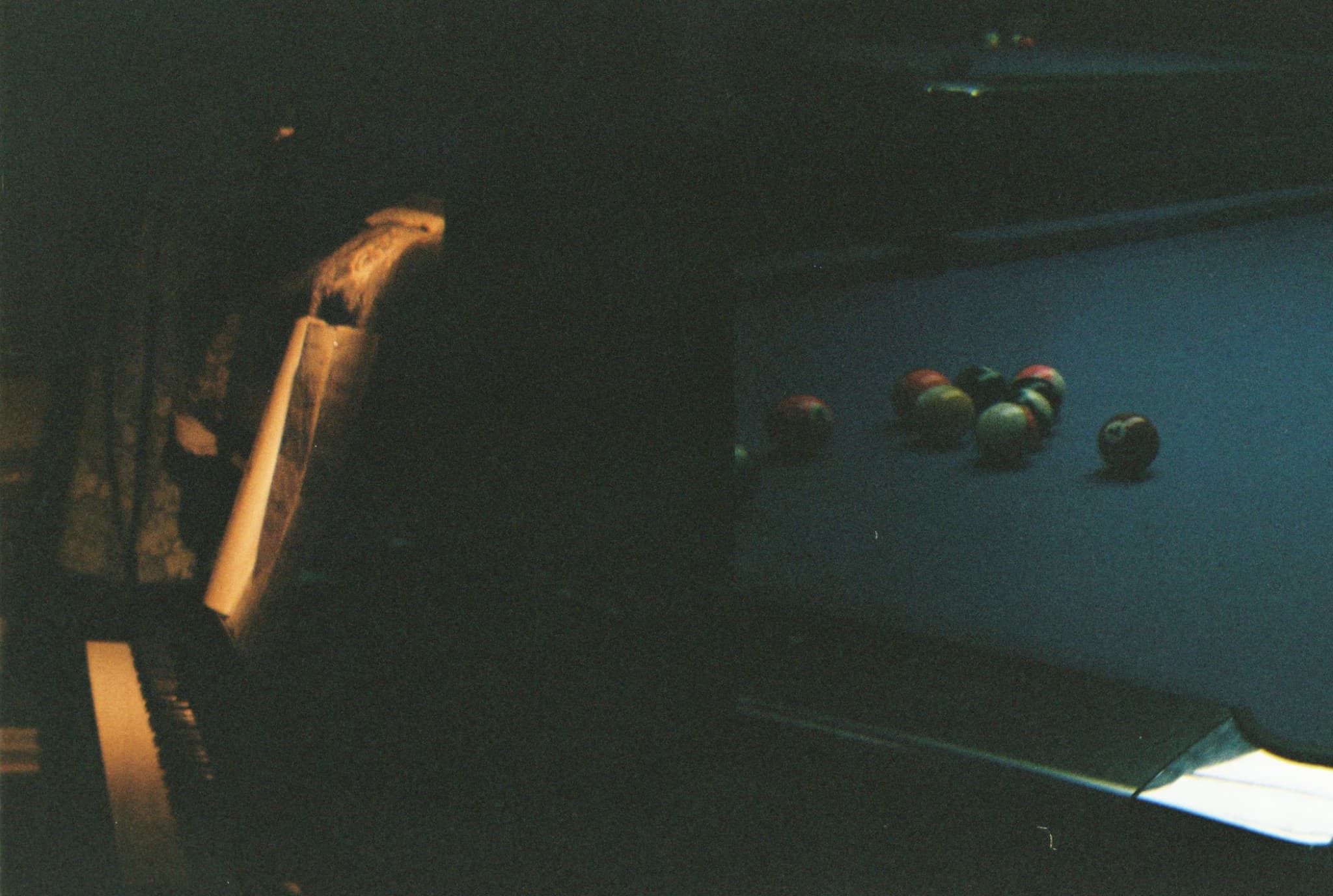 A dimly lit photograph shows billiard balls scattered on a pool table next to a piano.