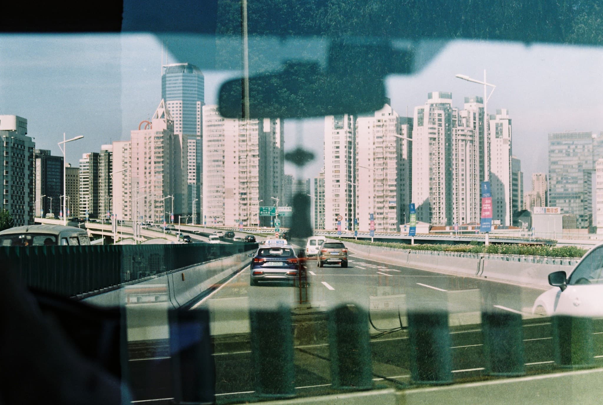 A view from inside a vehicle driving on a multi-lane city highway towards a dense skyline of tall white residential buildings.