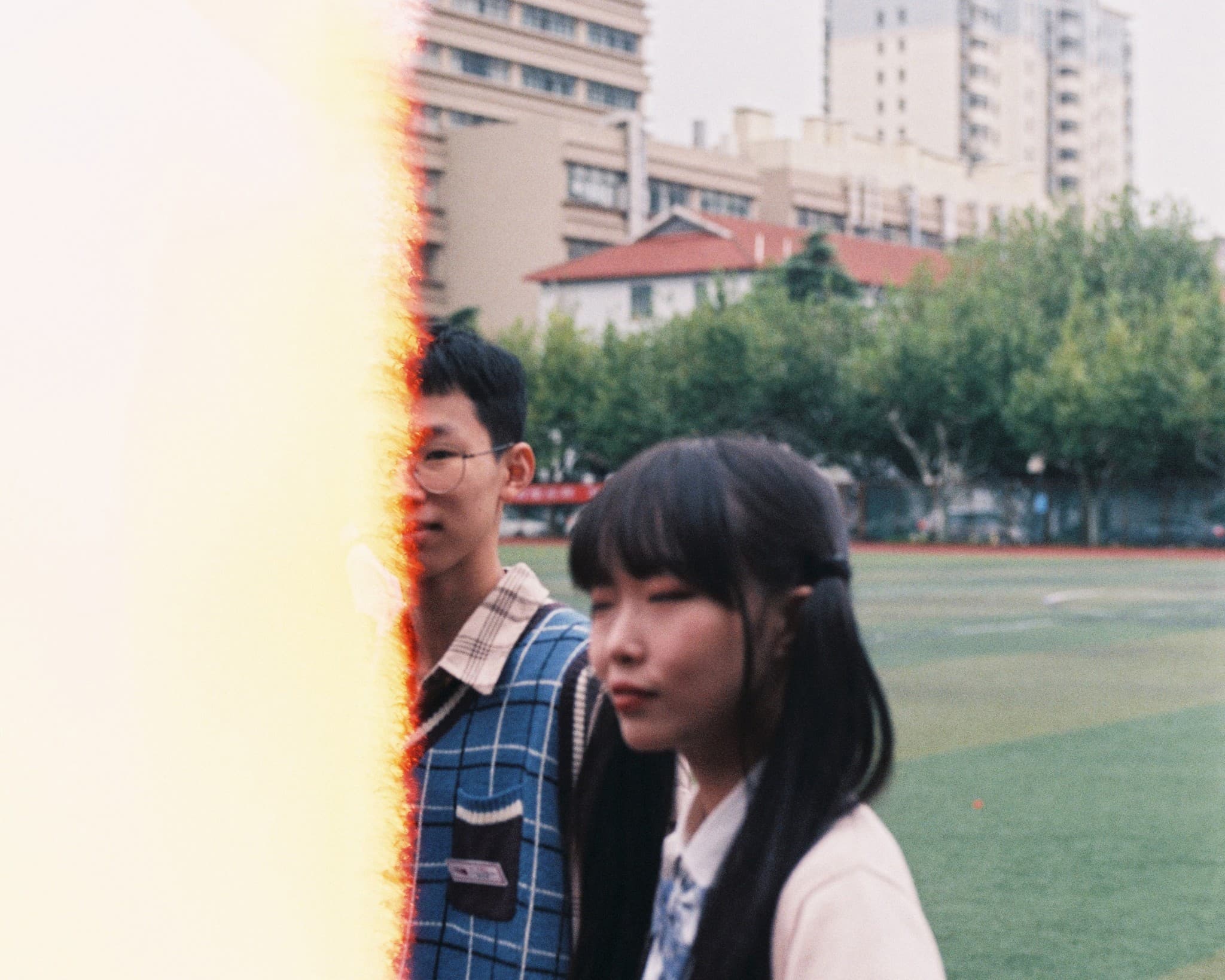 Two young students stand side-by-side on a green sports field, partially framed by a bright vertical light streak on the left side of the image.