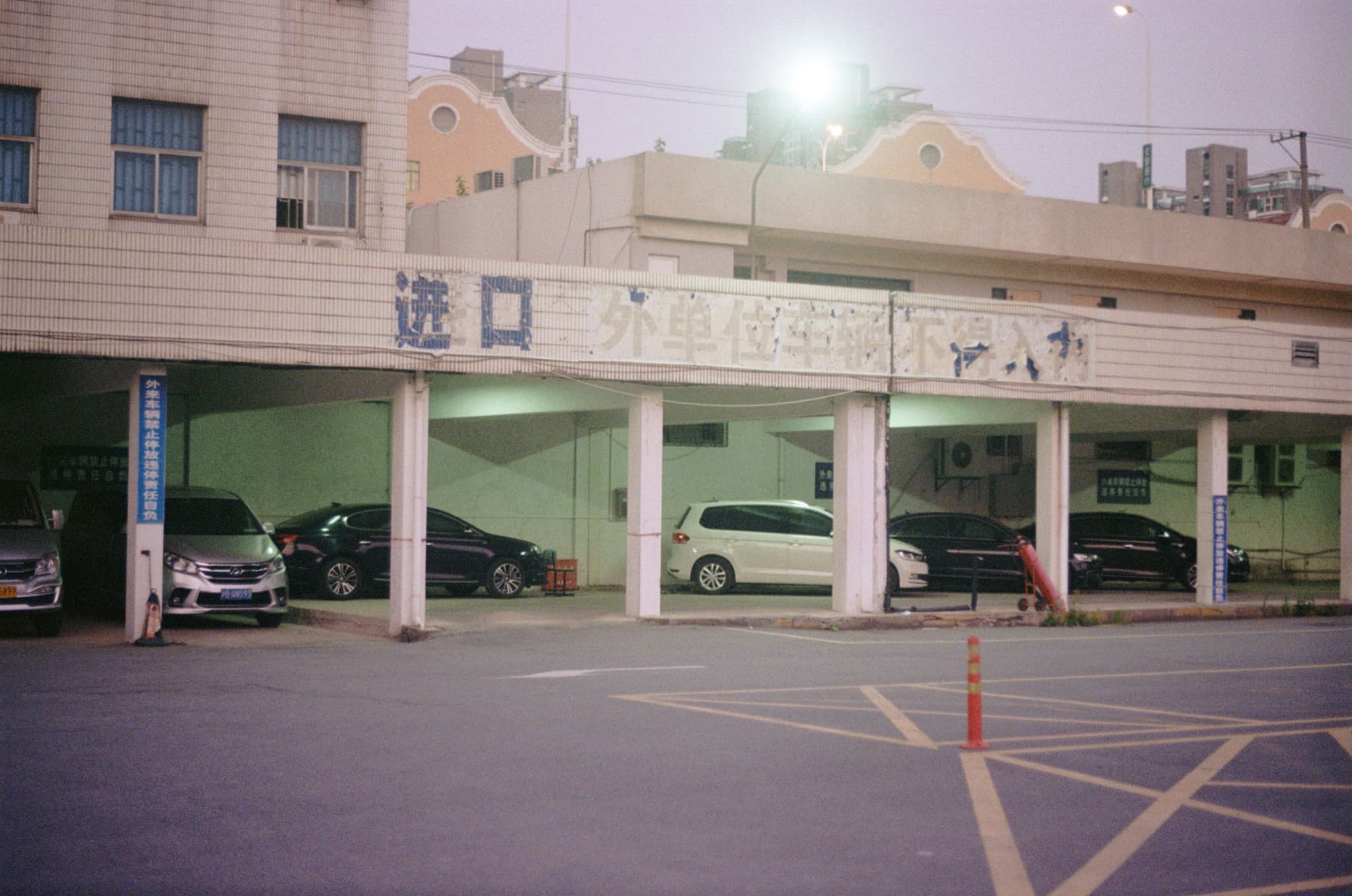 Several cars are parked underneath a covered parking structure featuring a long, faded sign with Chinese characters above the entrance.
