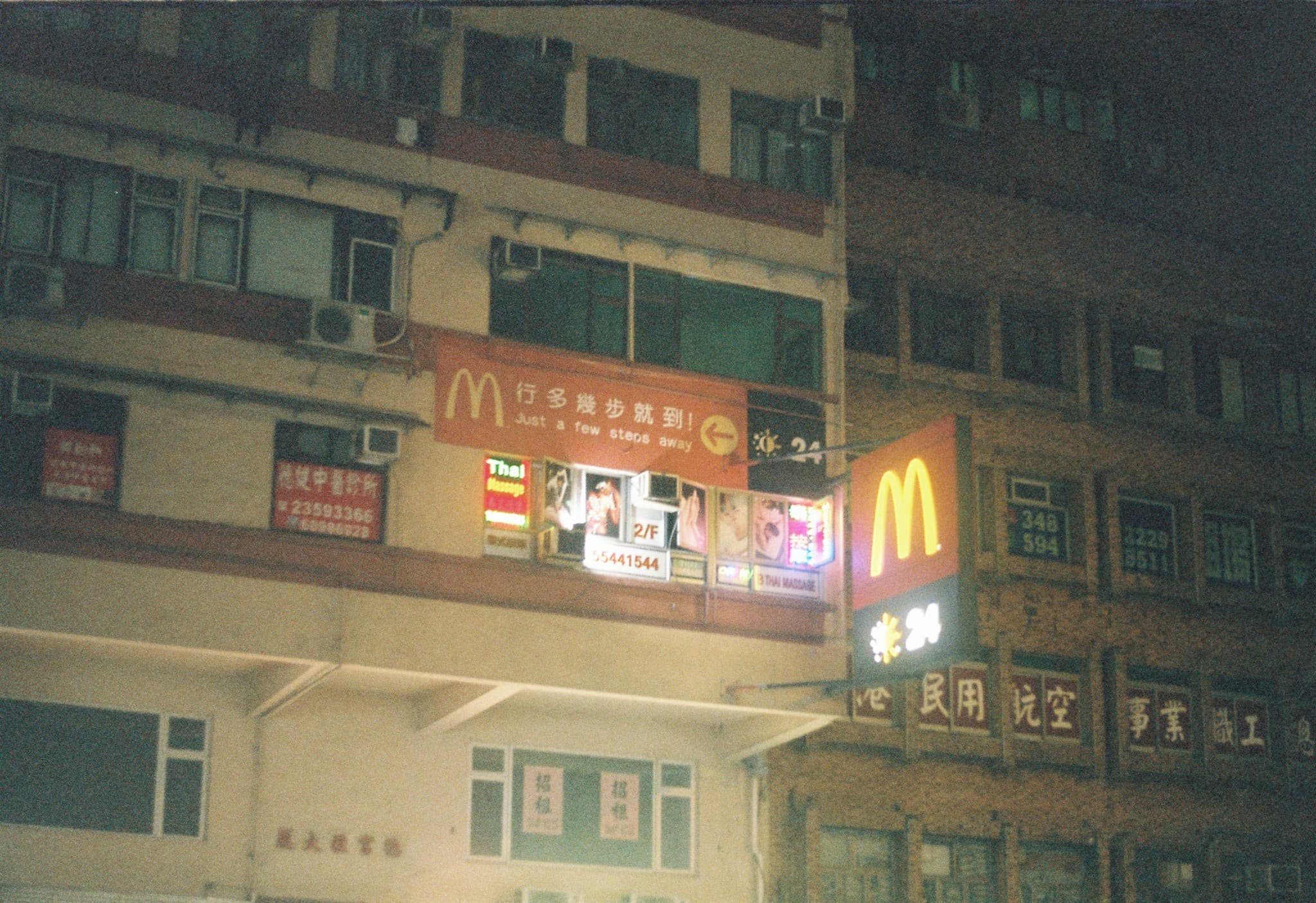 Nighttime view of building facades displaying illuminated signs for a McDonald's restaurant and a Thai massage parlor.