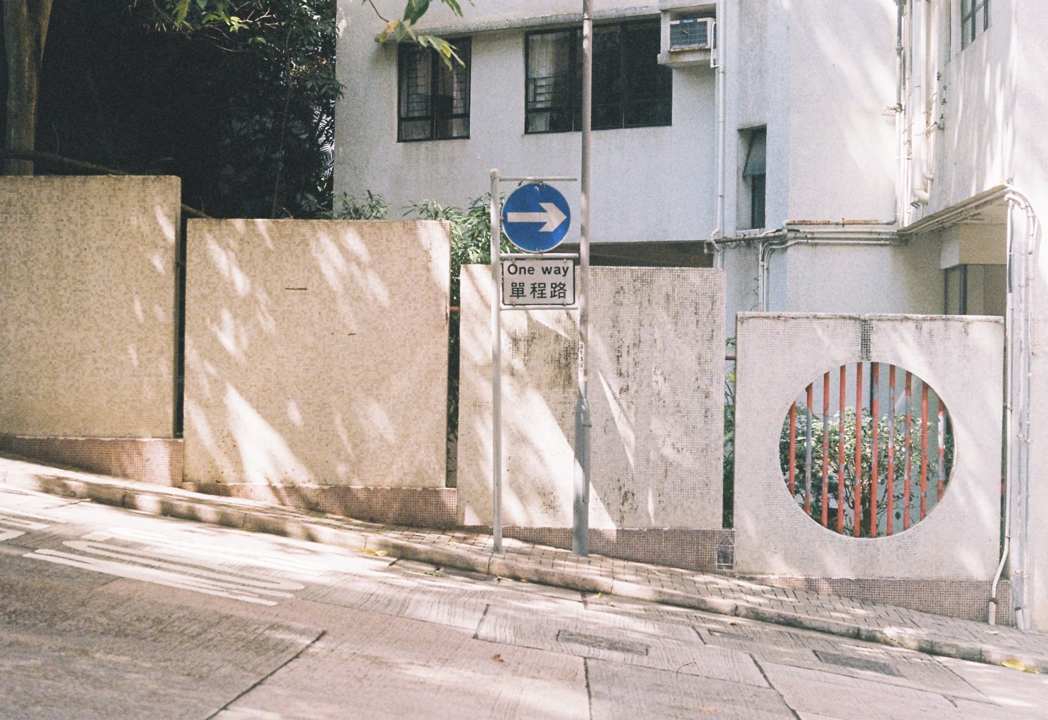 A sunny street view features a "One way" signpost standing in front of low beige walls and a white building in the background.