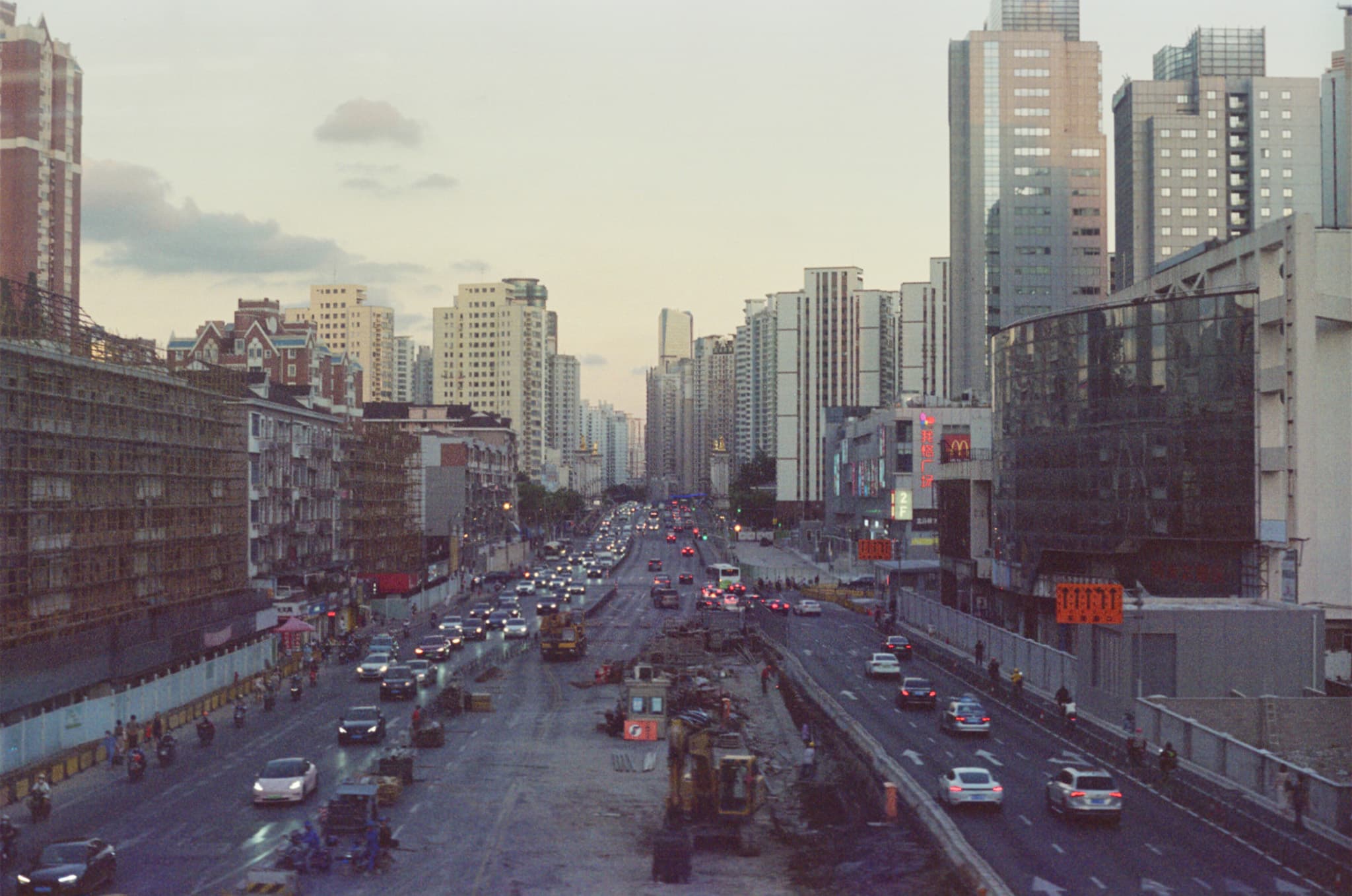 An elevated view of a busy city street with heavy traffic and construction work, flanked by tall buildings on both sides.