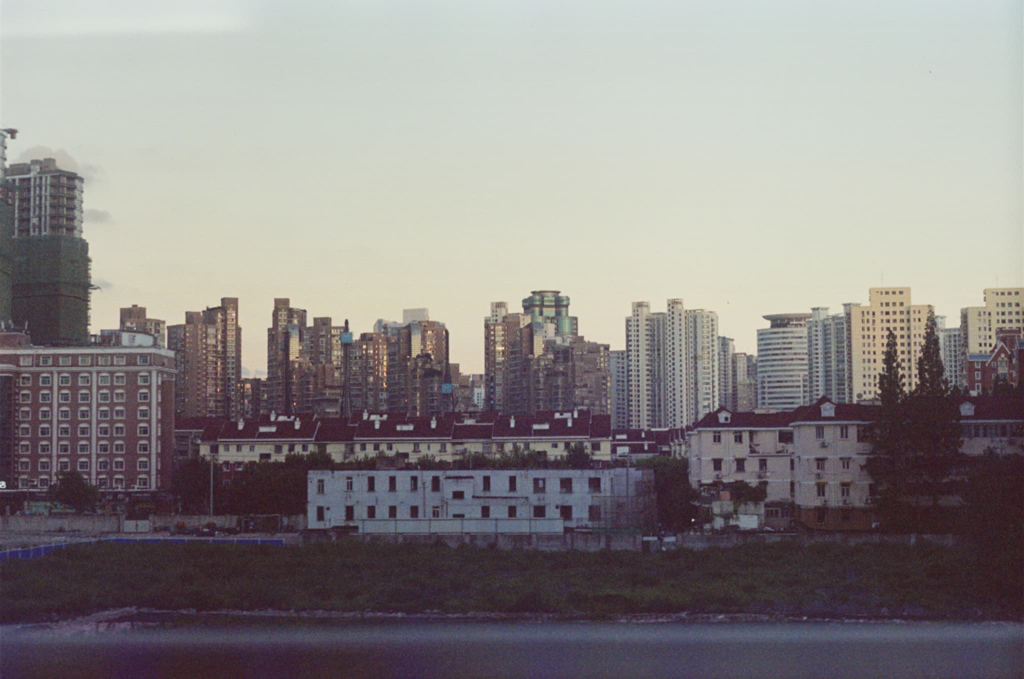 A cityscape view across a body of water showing low-rise residential buildings in the foreground and a dense cluster of high-rise skyscrapers in the background.