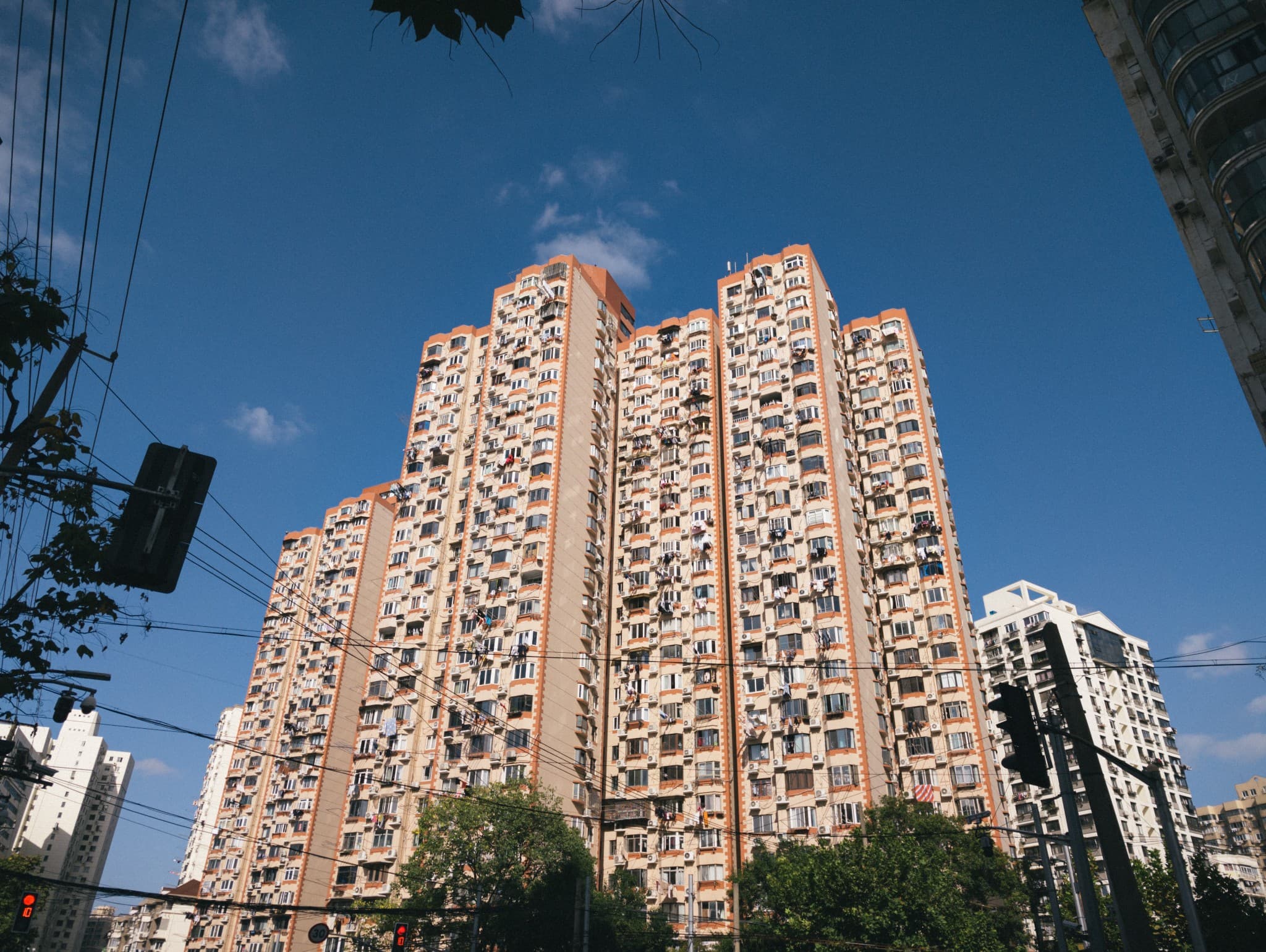 A low-angle view of a tall, beige apartment building with laundry hanging from windows set against a bright blue sky.